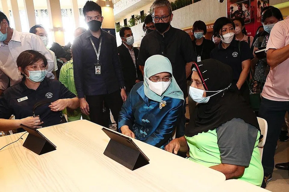 PERANTI IM-OK: Cik Khatihah, 81 tahun menunjukkan aplikasi yang seringkali digunakannya di dalam alat peranti IM-OK kepada Puan Halimah Yakob. - Foto BM oleh KELVIN CHNG