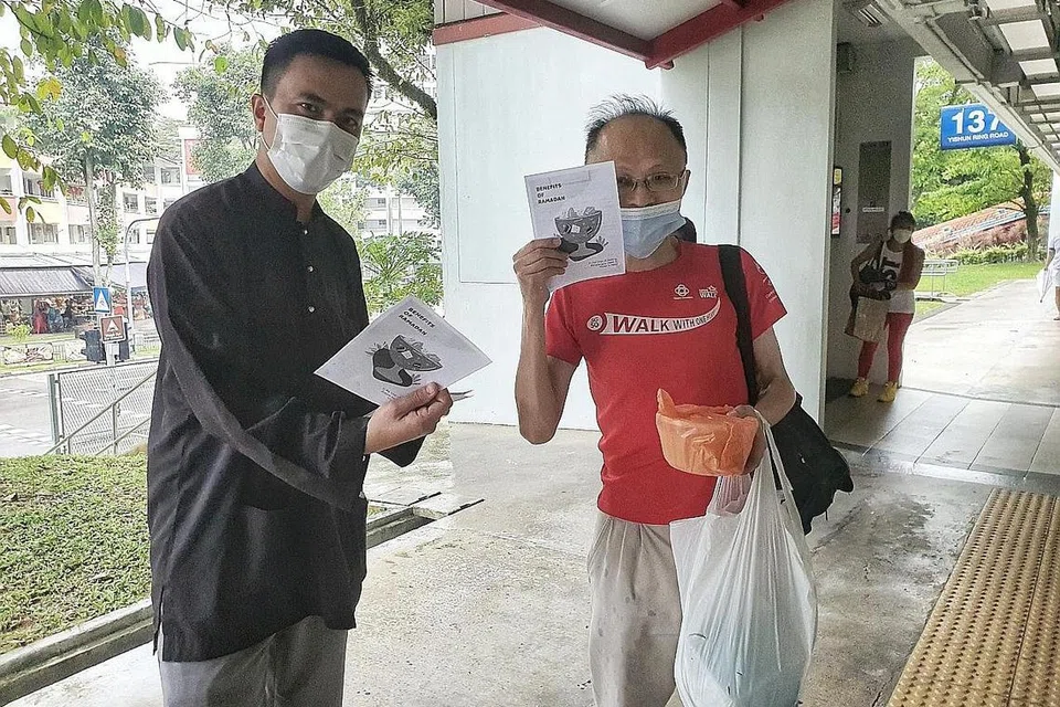 PENYAMPAIKAN MESEJ DI SEBALIK AMALAN PUASA: Ustaz Ruhaizan Abdullah (kiri) memberi risalah kepada penduduk bukan Melayu yang mendapat bubur Ramadan di Kolong Blok 137 Yishun Ring Road. Ia anjuran bersama Jawatankuasa Eksekutif Kegiatan Melayu (MAEC) Chong Pang. Foto MASJID DARUL MAKMUR
