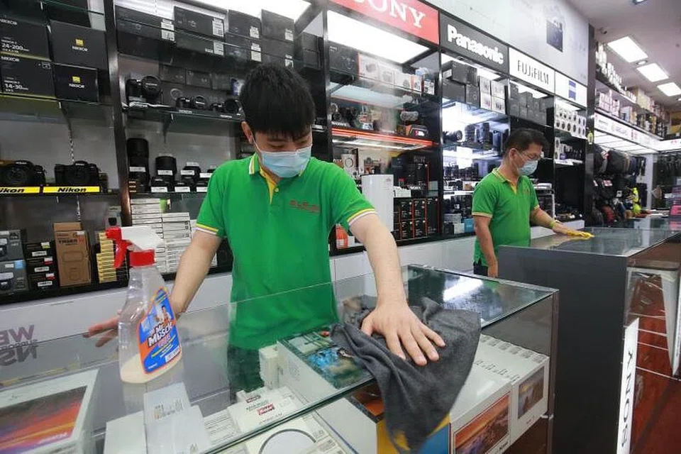 PEMBERSIHAN RAPI: Pekerja kedai kamera SLR Revolution di Pusat Beli-Belah Excelsior membersihkan kaunter yang sering disentuh pengunjung kedai sebagai langkah berjaga-jaga menyusuli pengesanan tiga kes Covid-19 di kedai itu. - Foto CHINESE MEDIA GROUP