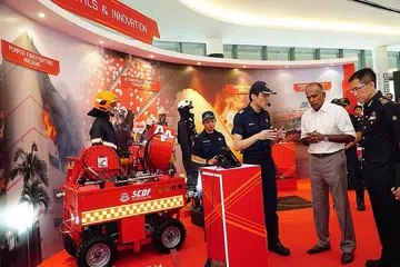 INOVASI BARU: Encik Shanmugam (berbaju kemeja) mendengar penerangan mengenai teknologi robotik untuk membantu anggota bomba dalam tugas mereka memadamkan kebakaran dan menyelamatkan nyawa. - Foto FACEBOOK/SCDF