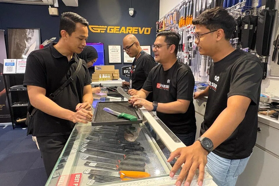 Pengurus Khidmat Pelanggan Tauke Pisau by Gearevo, Encik Muhammad Haris Hasnuddin (kanan),. dan Pengurus Operasi, Encik Adam Ariff (dua dari kanan) melayani pelanggan, Encik Muhammad Nadhir Adha Darus, dari Selayang, Selangor, untuk mengukir nama pada pisau melapah.