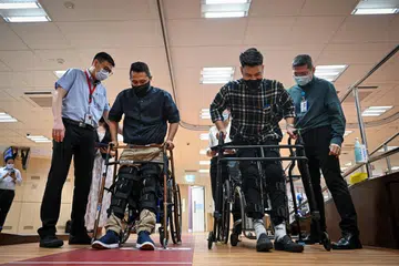 KEMBALI BERJALAN: Dua pesakit lumpuh, Encik Sam Subian dan Encik Asyraf Ghazali (dua dan tiga dari kiri), kini boleh ‘berjalan’ dengan penyeliaan selepas jalani satu percubaan oleh Hospital Tan Tock Seng dan Institut Neurosains Kebangsaan.