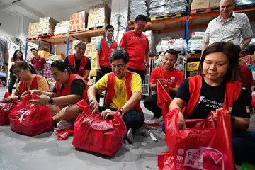 BERI KHIDMAT SUKARELA: Encik Desmond Lee (duduk, dua dari kanan) di acara membungkus makanan oleh sukarelawan di 'Food from the Heart'. Agihan $3,000, katanya, akan diberikan kepada setiap agensi khidmat sosial yang menganggotai Majlis Khidmat Sosial Kebangsaan (NCSS). - Foto BH oleh LIM YAOHUI