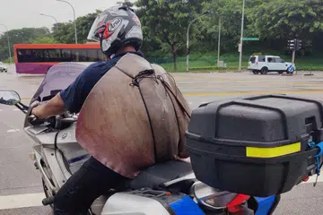 UMPAMA BEG: Encik Muhammad Sufiyan Jumali menunggang motosikalnya dengan membawa ikan pari hasil tangkapannya bak beg galas.