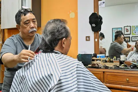 Encik Hamzah menggunting rambut pelanggan setia, Encik Abdul Kadir, yang sudah mengunjungi kedai gunting, Bugs Bunny, selama lebih 20 tahun.