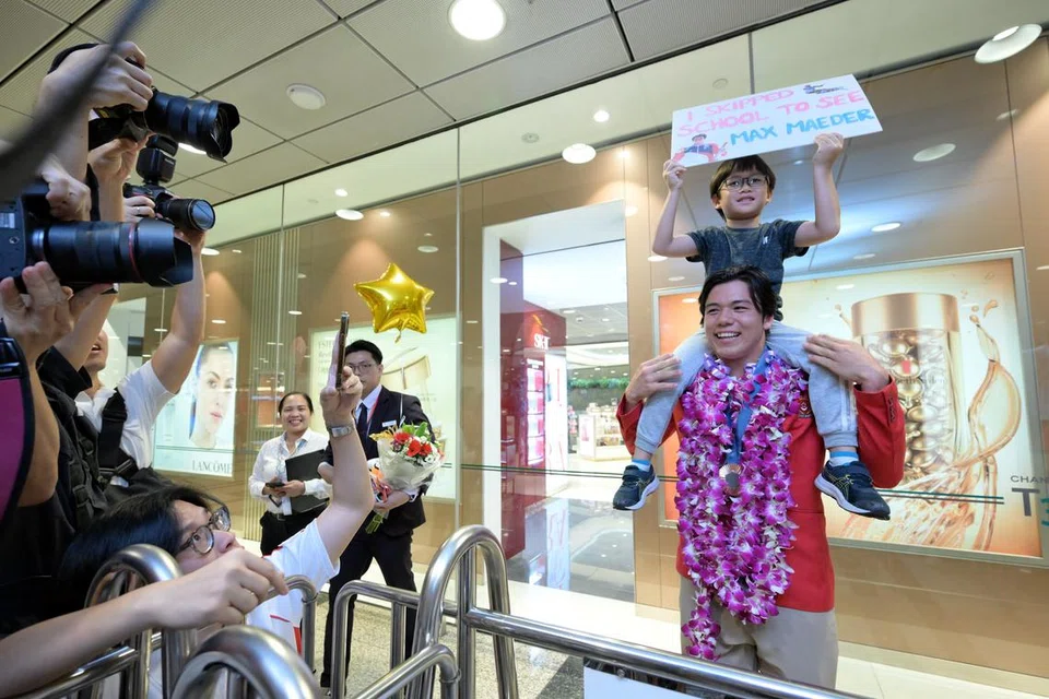 Atlet luncur lelayang, Maximilian Maeder (tengah), meletakkan salah seorang peminatnya, Caleb Tan, enam tahun, di atas bahunya, yang datang untuk menyambutnya pulang dari Paris di Terminal 3 Lapangan Terbang Changi pada 13 Ogos.