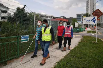 PEMANDU JADI SAHABAT: (Dari kiri) Encik Edwin Khoo, dipandu oleh Encik S.M. Liton, dan Encik Kelvin Tan dipandu oleh Encik Periyasami Vasanthakumar sedang mereka berjalan menuju stesen MRT Caldecott. Pekerja asing dikerah oleh Samsung C&T sebagai pemandu kepada pejalan kaki cacat penglihatan, dan juga bagi mengawasi penumpang kereta api di sekitar kawasan pembinaan di stesen berkenaan. - Foto-foto BM oleh KUA CHEE SIONG