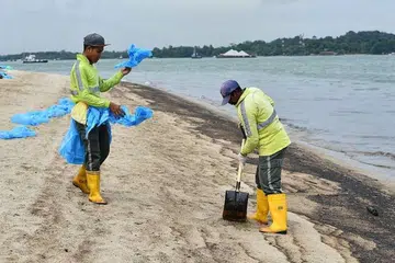 Kontraktor NEA daripada Ramky Cleantech Services Pte Ltd membersihkan pasir daripada kesan minyak di Pantai Changi pada 5 Jan. 