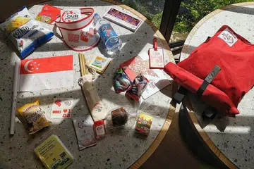 BERANEKA BARANG DAN MAKANAN: Barangan yang dimuatkan dalam beg cenderamata NDP 2019 boleh digunakan semula, seperti penyedut dibuat daripada buluh dan kipas. Penonton juga boleh makan cemil-cemilan seperti biskut, roti, mufin dan kentang goreng. - Foto BH oleh MARK CHEONG
