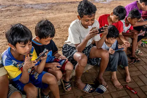 Kanak-kanak menggunakan telefon bimbit di tepi jalan di Jakarta pada 27 November.