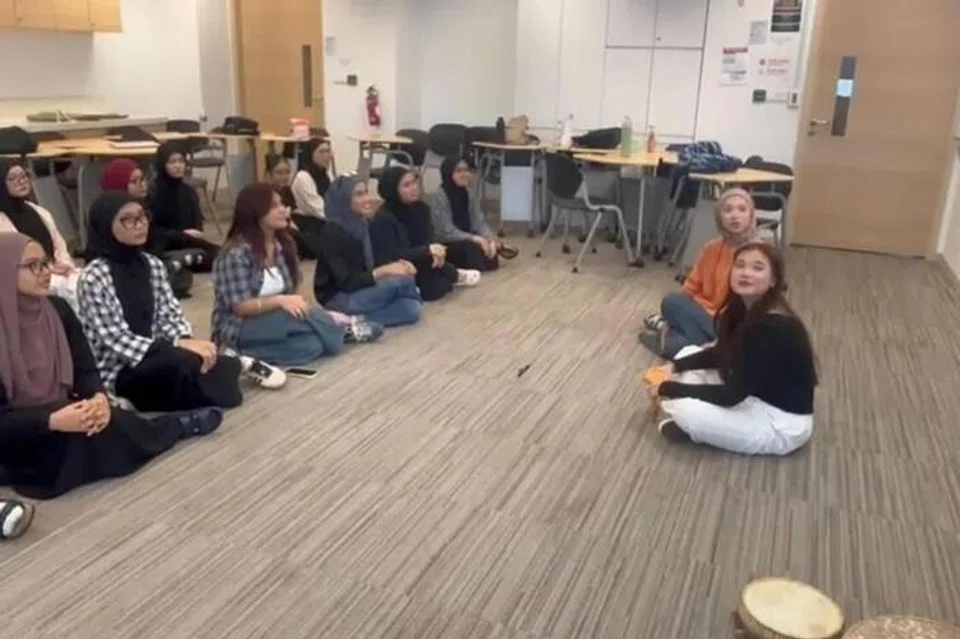 Sebagai sebahagian daripada modul Pengajaran Bahasa Melayu melalui Seni, Cik Dinah Syaqilah (berbaju jingga) diperkenalkan kepada seni persembahan tradisional Melayu seperti dikir barat, iaitu persembahan beramaian yang rancak.