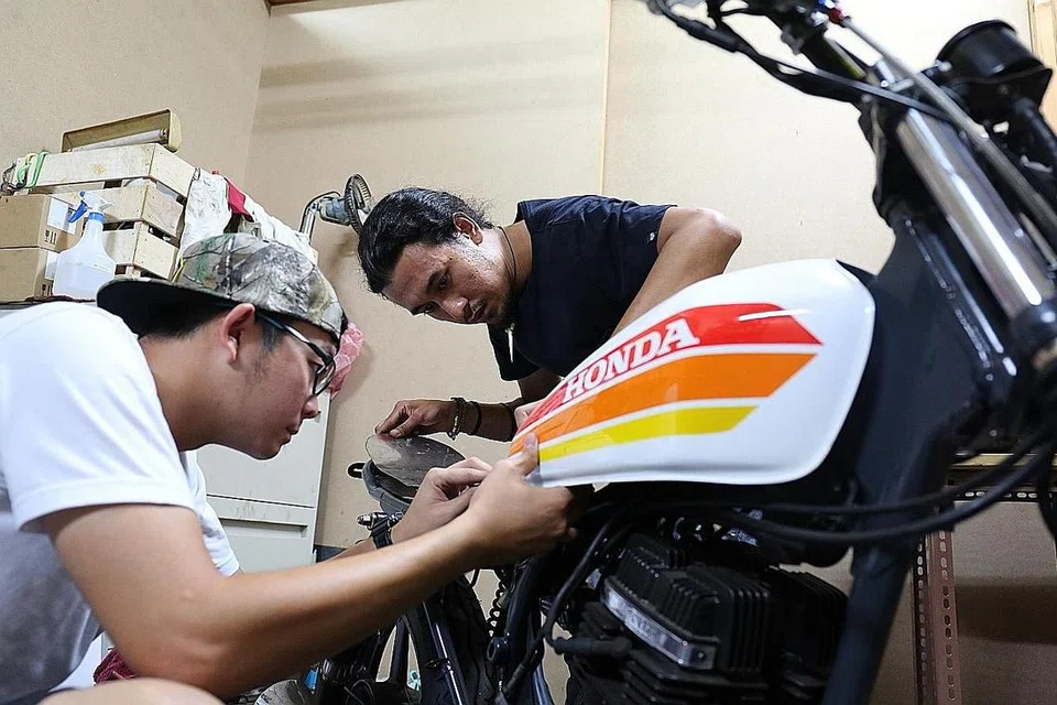 'HIDUPKAN' KEMBALI MOTOSIKAL KLASIK: Encik Loh (kiri) dan Encik Rusydi sedang memasang tangki minyak motosikal yang telah mereka ubah suai agar kelihatan lebih 'old school'. - Foto-foto FAKHRURADZI ISMAIL