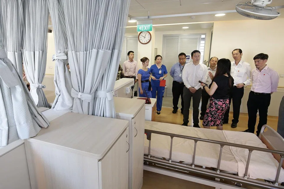 ELAK PESAKIT JATUH: Dr Lam Pin Min (lima dari kanan) mendengar penjelasan tentang operasi huraian pengurusan pencegahan jatuh yang kini sedang diuji di Pusat Penjagaan Orange Valley di Balestier semalam. Sistem itu dapat mengesan pergerakan pesakit atas katil dan akan memaklumkan kepada kakitangan menerusi aplikasi telefon bimbit jika ada pesakit yang bangun dan cuba turun dari katilnya. - Foto BH oleh DARWIS SUNARYO