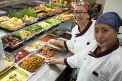 TUNGGAK GERAI: Dua beradik ini, Cik Suriati (kanan) dan kakaknya, Cik Sulami (berkaca mata) memanfaatkan 'kekuatan' masing-masing untuk sama-sama menguruskan gerai Warong Anak Wedok yang menyediakan pelbagai jenis lauk-pauk.ini. - Foto BH oleh SYAMIL SAPARI