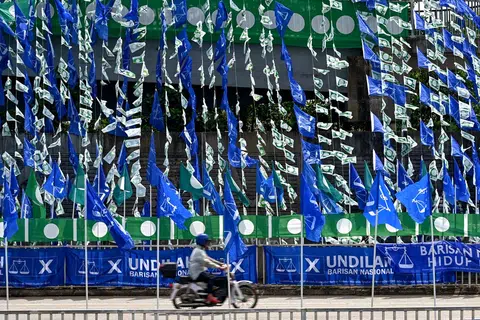 KIAN RANCAK: Seorang penunggang motosikal berlalu di depan deretan bendera Barisan Nasional (biru) dan bendera Parti Islam SeMalaysia yang digantung di jejantas di Kampung Bukit Guntung, Kuala Terengganu.