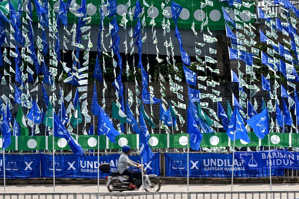 KIAN RANCAK: Seorang penunggang motosikal berlalu di depan deretan bendera Barisan Nasional (biru) dan bendera Parti Islam SeMalaysia yang digantung di jejantas di Kampung Bukit Guntung, Kuala Terengganu.