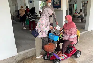 PELUANG BERAMAH MESRA DENGAN PENDUDUK: Cik Selina Salleh (kiri) bersama Ustaz Ruhaizan Abdullah (tengah) bertanya khabar kepada Cik Hasnah Wahab yang menaiki PMD, untuk mengambil bubur di kolong Blok 137 Yishun Ring Road anjuran bersama Jawatankuasa Eksekutif Kegiatan Melayu (MAEC) Chong Pang dan pihak Masjid Darul Makmur. - Foto MASJID DARUL MAKMUR