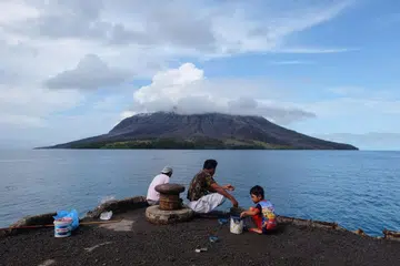 Orang ramai menangkap ikan di pelabuhan di pulau Tagulandang di Sitaro, Sulawesi Utara pada 19 April 2024, ketika gunung berapi Gunung Ruang dilihat di latar belakang mengeluarkan asap.