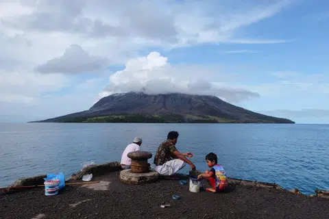 Orang ramai menangkap ikan di pelabuhan di pulau Tagulandang di Sitaro, Sulawesi Utara pada 19 April 2024, ketika gunung berapi Gunung Ruang dilihat di latar belakang mengeluarkan asap.