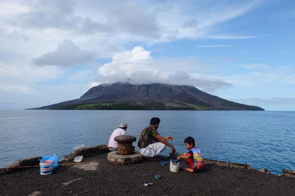 Orang ramai menangkap ikan di pelabuhan di pulau Tagulandang di Sitaro, Sulawesi Utara pada 19 April 2024, ketika gunung berapi Gunung Ruang dilihat di latar belakang mengeluarkan asap.