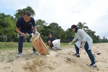 BERSIHKAN PANTAI: Encik Mohd Fahmi Aliman (kiri) bersama relawan Sharifah Sheikha Haroon Aljunied dan anaknya, Encik Daniyal Rashad Mohammad Yusri, mengutip sampah di pantai East Coast semasa kegiatan membersihkan pantai anjuran CDC South East semalam. - BH oleh * ALPHONSUS CHERN