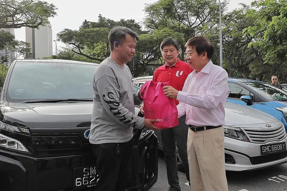SUMBANGAN TANDA PENGHARGAAN: Encik Khaw Boon Wan (kanan) yang didampingi Setiausaha Agung Kongres Kesatuan Sekerja Kebangsaan (NTUC), Encik Ng Chee Meng (tengah) menyampaikan beg habuan kepada seorang pemandu kereta sewa privet, Encik Gabriel Goh, di Pusat Makanan Newton semalam. 
