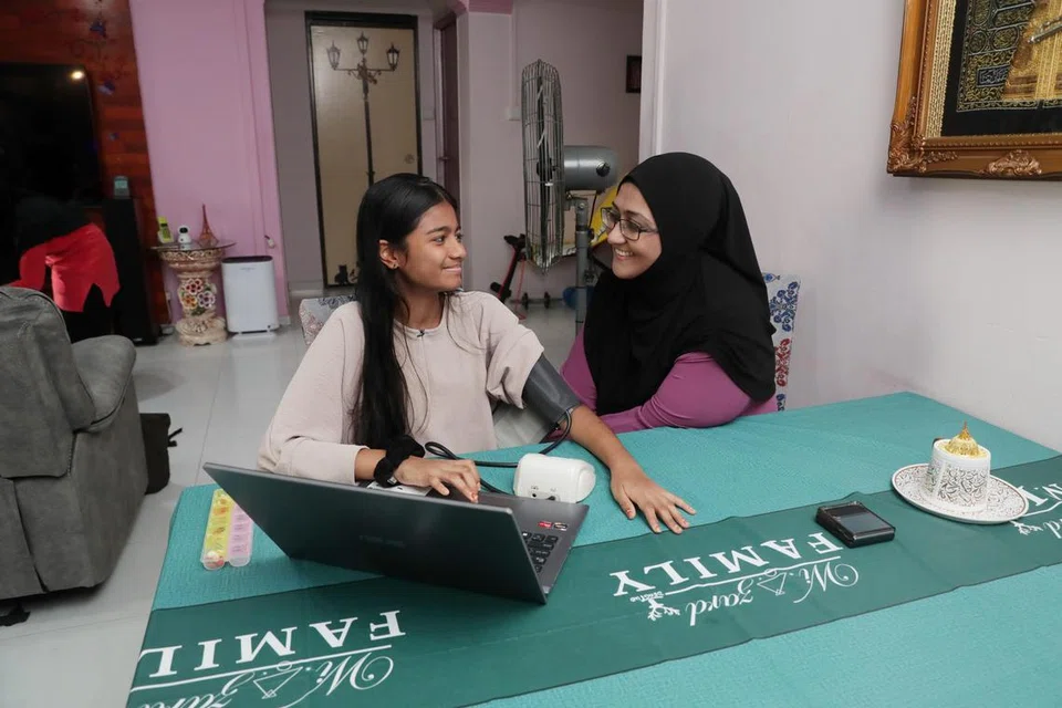 SELESA DI RUMAH: Nur Sameera Begum Shaik Sulaiman (kiri) ialah antara pesakit MIC@Home yang menerima penjagaan di rumah. Ibunya, Nurzahirah Sulaiman (kanan), membantunya menggunakan peralatan perubatan untuk memantau kesihatannya.