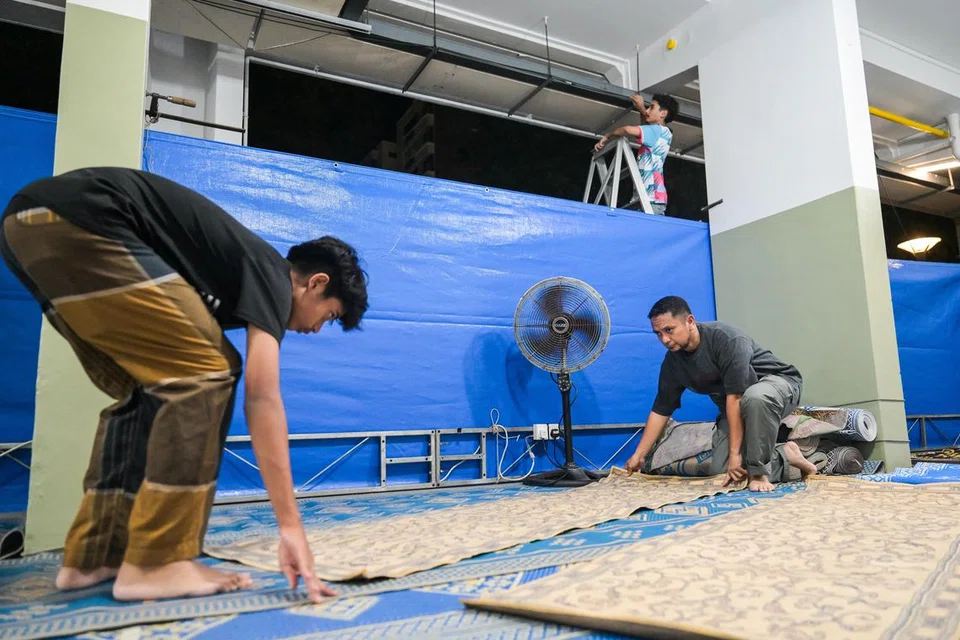 Sukarelawan Jawatankuasa Kejiranan Islam Simei (JKIS), Encik Ahmad Azadee Mawasi (kanan), 51 tahun, bersama dua anaknya, Sharif Hidayatullah Ahmad Azadee (kiri), 15 tahun, dan U’bayd Ijaaballah Ahmad Azadee, 18 tahun, menyiapkan ruang solat tarawih di kolong Blok 116, Simei Street 1, pada 27 Februari. 