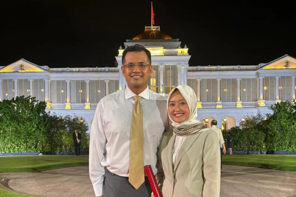 Menteri Negara (Perhubungan dan Penerangan merangkap Kesihatan), Cik Rahayu Mahzam, bergambar bersama suaminya, Encik Muhamad Imaduddien Abd Karim, di depan Istana. Cik Rahayu berpakaian sut berwarna cerah, sepadan dengan tali leher suaminya yang berwarna krim.