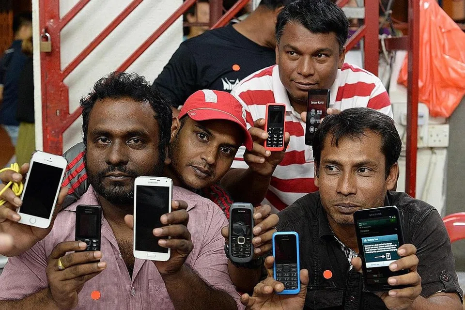 TUKAR TELEFON BARU: Pekerja asing menunjukkan telefon bimbit 2G (yang mempunyai butang) yang telah ditukar kepada telefon bimbit 3G (dengan skrin sentuhan) di bawah usaha TWC2. - Foto AFP