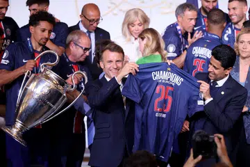 Presiden Perancis, Emmanuel Macron (depan, dua dari kanan) dan presiden Paris Saint Germain (PSG) Nasser al-Khelaifi (kanan) memegang jersi PSG ketika pemain pertahanan PSG, Marquinhos (kiri), memegang trofi Liga Juara-Juara semasa sambutan kemenangan mereka di Istana Élysée pada 1 Jun. Namun, Macron mengecam para peminat yang keterlaluan menyambut kemenangan tersebut hingga timbul keganasan semasa sambutan mereka di kota Paris.