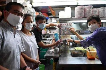 STATUS BARU: Menteri Kebudayaan, Masyarakat dan Belia, Encik Edwin Tong (kiri), bersama Menteri Kemampanan dan Sekitaran, Cik Grace Fu (kanan), mengagihkan label yang menunjukkan budaya penjaja kini disertakan dalam Senarai Wakil Unesco Warisan Budaya Bagi Kemanusiaan Yang Tidak Ketara di Pusat Makanan Ghim Moh semalam. - Foto BH oleh CHONG JUN LIANG