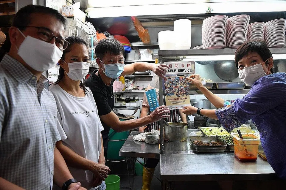 STATUS BARU: Menteri Kebudayaan, Masyarakat dan Belia, Encik Edwin Tong (kiri), bersama Menteri Kemampanan dan Sekitaran, Cik Grace Fu (kanan), mengagihkan label yang menunjukkan budaya penjaja kini disertakan dalam Senarai Wakil Unesco Warisan Budaya Bagi Kemanusiaan Yang Tidak Ketara di Pusat Makanan Ghim Moh semalam. - Foto BH oleh CHONG JUN LIANG