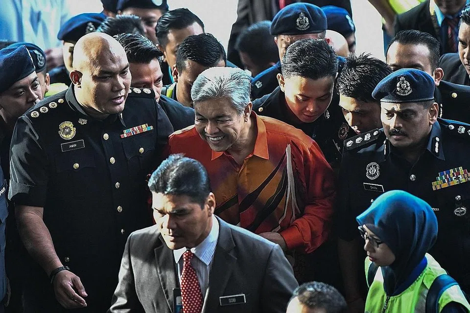 MAHU TERUS BERKHIDMAT: Datuk Seri Dr Ahmad Zahid Hamidi (baju oren) diiring pegawai polis ke mahkamah di Kuala Lumpur untuk menghadapi tuduhan pada 19 Oktober lalu. Datuk Zahid bertegas enggan menggundurkan diri sebagai Presiden Umno sedang kesnya dibicarakan. - Foto AFP