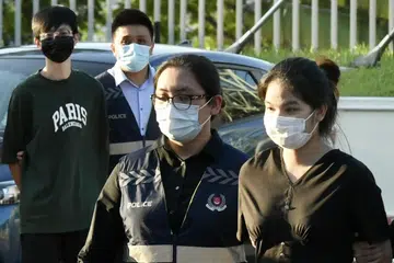 Pasangan suami isteri yang terlibat dalam penipuan barangan mewah, Pi Jiapeng dan Pansuk Siriwipa, diiringi pegawai polis di Pusat Pemeriksaan Woodlands pada 11 Ogos 2022.