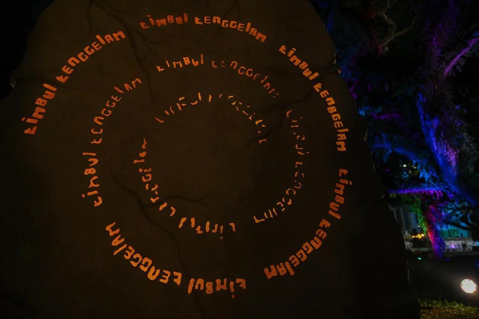 Seni pemasangan ‘Batu Ghaib’ ini menonjolkan seni kata jampi “timbul tenggelam” yang terlakar dan bercahaya pada arca Batu Bersurat Singapura.