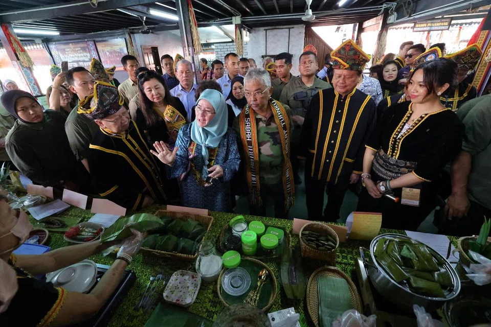 CUBA MAKANAN TRADISIONAL: Sultan Abdullah Ahmad Shah dan Tunku Azizah Aminah Maimunah Iskandariah (tiga dan empat dari anan) mencuba pelbagai jenis makanan tradisional ketika melawat Perkampungan Budaya, Persatuan Kebudayaan Kadazadusun (KDCA) Penampang di Sabah.