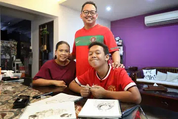 LEBIH YAKIN: Nuh Syazwan (kanan) tidak pernah jadikan masalah disleksia sebagai hambatan baginya melakukan kegiatan melukis yang merupakan hobinya. Dia sering dapat sokongan keluarga termasuk ibu bapanya, Encik Muhammad Zulkarnaen dan ibunya Cik Siti Zakiah. - Foto BH oleh GAVIN FOO