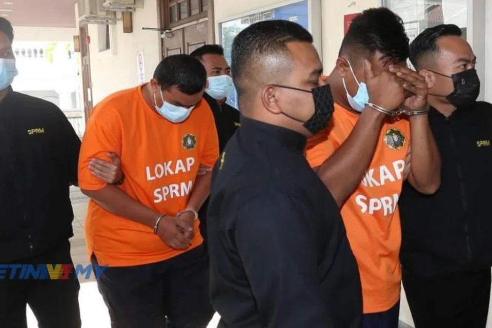 Dua anggota polis Unit Rondaan Bermotosikal (berbaju oren) diiringi pegawai Suruhanjaya Pencegahan Rasuah Malaysia (SPRM) ketika ditahan reman bagi membantu siasatan berhubung kes rasuah di Mahkamah Majistret Georgetown, Pulau Pinang, pada 20 April.