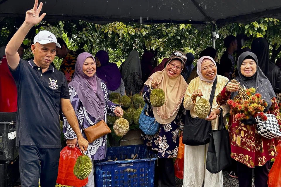 Encik Samsul Kamarudin, 52 tahun (kiri), bersama pengunjung warga Singapura yang membeli buah durian untuk dibawa pulang.