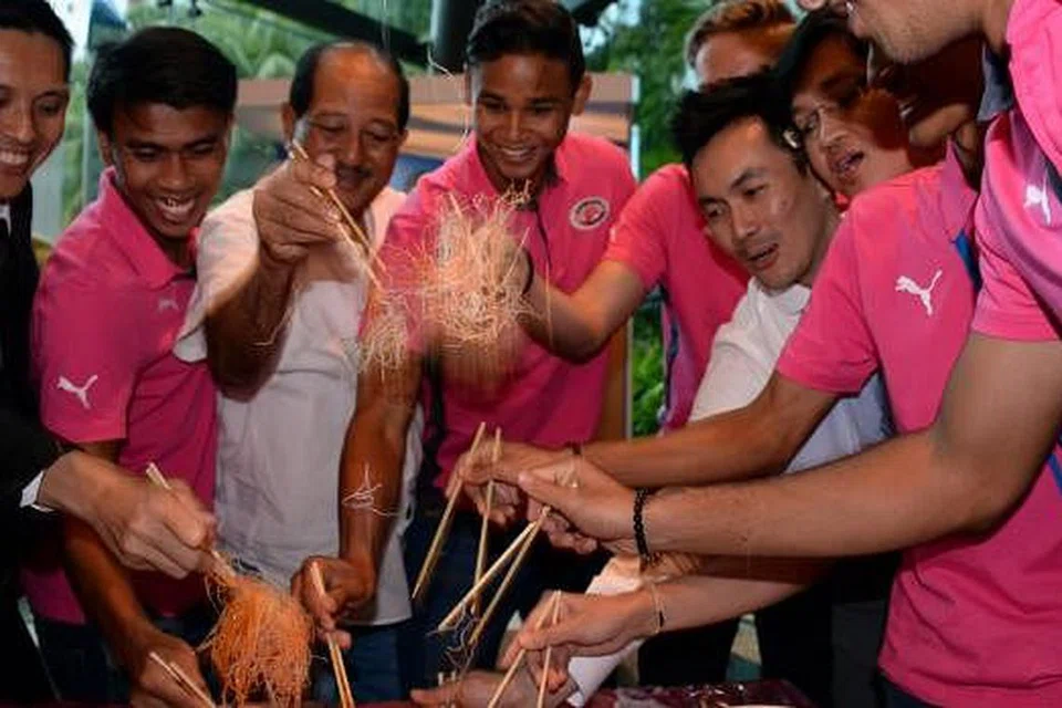 HARAPAN BARU HOME UNITED: Jurulatih Philippe Aw (kiri) mengadakan upacara melambung yusheng bersama pasukannya sebagai tanda kemakmuran pada musim Liga-S baru ini. - Foto ZAINAL YAHYA