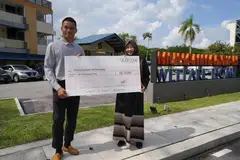 Penjaga gawang Singapura, Hassan Sunny,  menyerahkan cek bernilai $10,000 kepada Ketua Rumah Kebajikan Muhammadiyah, Cik Rahmatunnisa Abdul Majeed (kanan).
