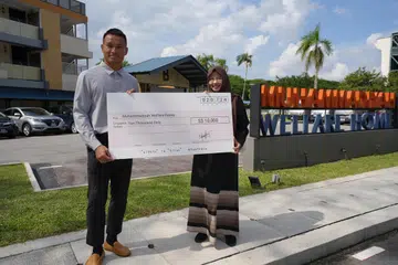 Penjaga gawang Singapura, Hassan Sunny,  menyerahkan cek bernilai $10,000 kepada Ketua Rumah Kebajikan Muhammadiyah, Cik Rahmatunnisa Abdul Majeed (kanan).