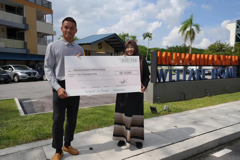 Penjaga gawang Singapura, Hassan Sunny,  menyerahkan cek bernilai $10,000 kepada Ketua Rumah Kebajikan Muhammadiyah, Cik Rahmatunnisa Abdul Majeed (kanan).