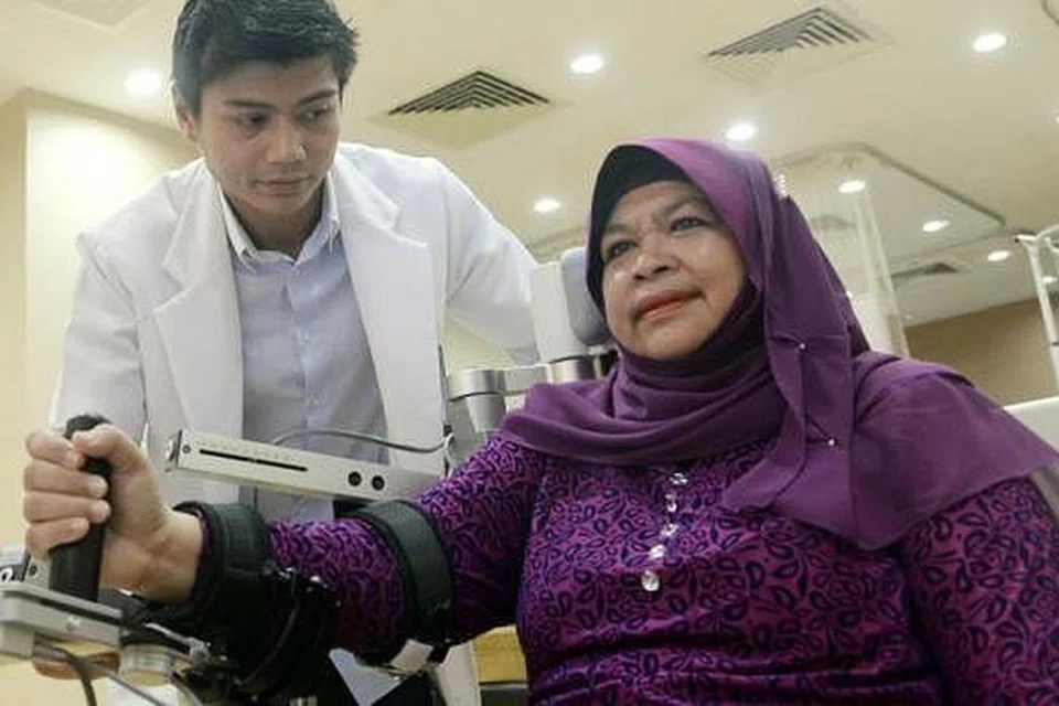 TERAPI GUNA MESIN: Jika dahulu tangan kanannya berasa lemah, kini Cik Hawa yang menggunakan mesin ArmeoSpring sambil diperhatikan Pakar Terapi Okupasional Kanan Jabatan Terapi Okupasional TTSH, Encik Damiri Hosain, berasakan beliau sudah 90 peratus pulih daripada masalah angin ahmar yang dialaminya tahun lalu. - Foto TAUFIK A. KADER