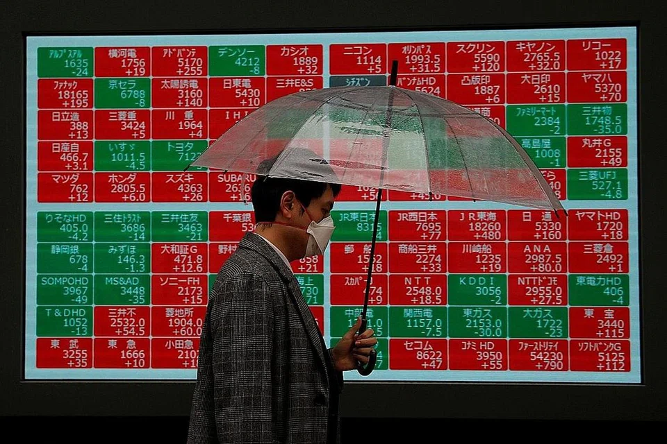 MENJUNAM: Seorang lelaki yang memakai pelitup berjalan di depan papan tanda pasaran saham di Tokyo yang menunjukkan banyak kaunter saham mengalami kemerosotan. - Foto REUTERS.