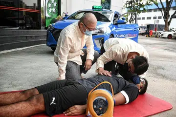 UPAYA RESPONS DENGAN CEPAT: Pemandu teksi Comfort DelGro, Encik Irmansah Azir (kanan) dan Cik Foo Mui Leng, yang telah menjalani latihan Program Kesediaan Kecemasan Masyarakat (CEPP) oleh SCDF, melakonkan prosedur bantuan kecemasan bagi menyedarkan semula seorang 'mangsa' serangan jantung. - Foto BH oleh KUA CHEE SIONG