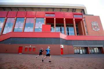 Dua orang berlari anak di luar Stadium Anfield di Liverpool pada 14 Mac. Perlawanan Liverpool dengan Crystal Palace pada hujung minggu ini telah digantung kepada tarikh selepas 3 April, seperti semua perlawanan Liga Perdana England yang lain. 