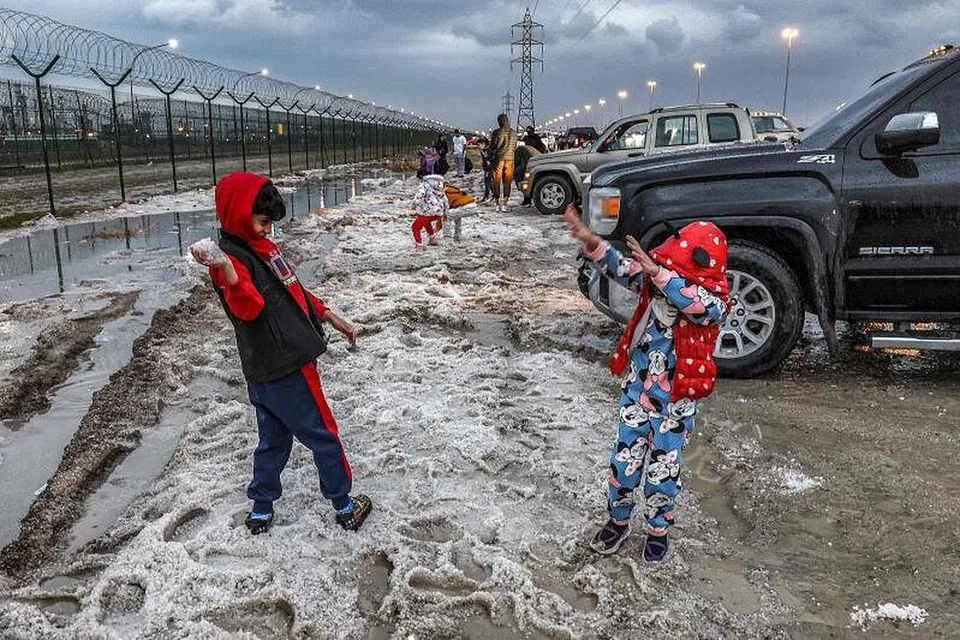 BERMAIN DENGAN AIS BATU: Kanak-kanak memakai baju hujan sedang mereka bermain dengan ais batu di daerah Umm al-Haiman, kira-kira 50 kilometer ke selatan Kuwait City. 