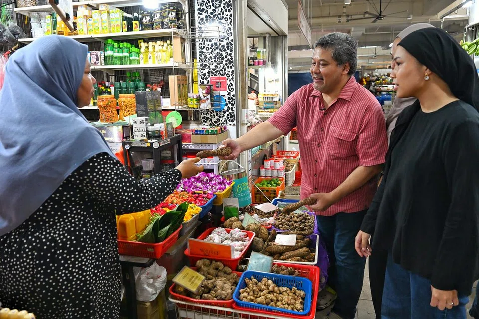 Encik Suryakenchana Omar (tengah) bersama dua anaknya, Cik Nur Tiara Kenchana (terselindung) dan  Cik Kamelia Tufah Kenchana (kanan) sering membeli bahan-bahan membuat jamu daripada Cik Siti Norhuda Saleh (kiri) di Pasar Geylang Serai. 